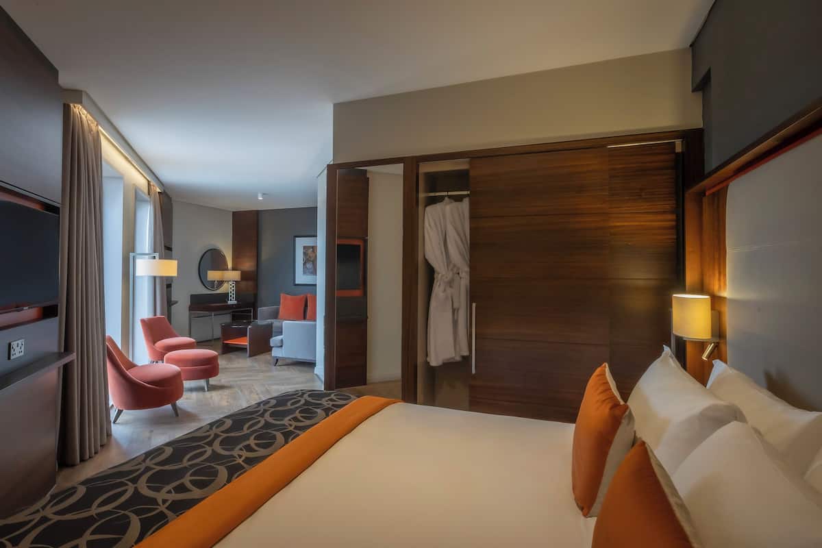 Ein Hotelzimmer mit einem großen Bett, einem Schreibtisch mit Stuhl, einem Fernseher und einem Bademantel, der an einer Holztür hängt.