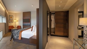 Ein modernes Hotelzimmer mit einem Bett, einer Sitzecke mit Stuhl und Tisch, einem Kleiderschrank und einem Badezimmer mit Glastrennwand.