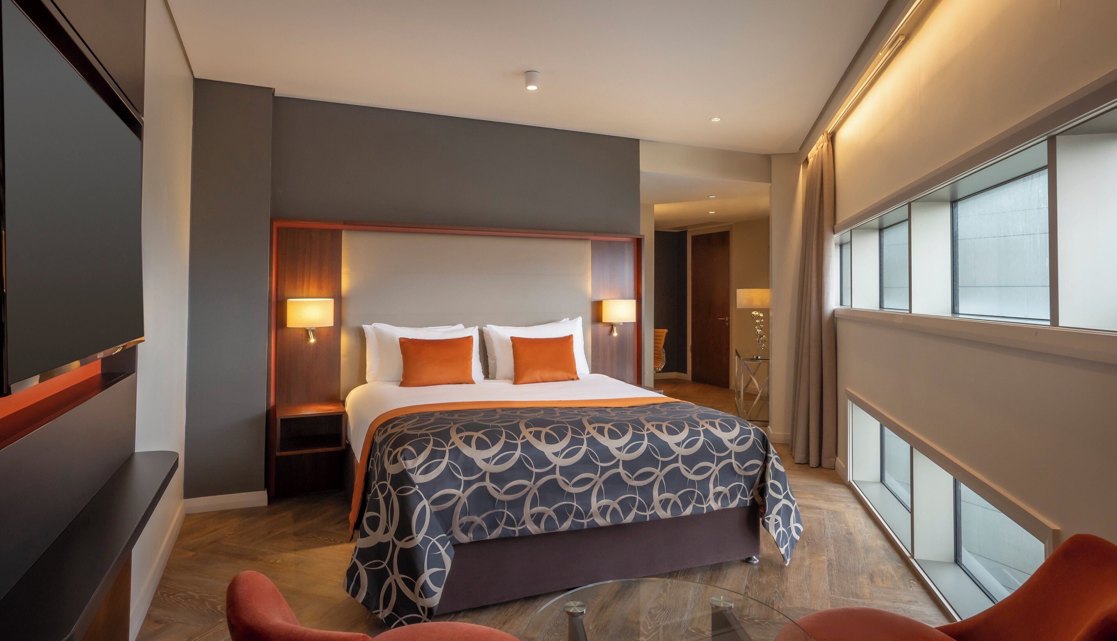 A hotel room with a large bed, two bedside lamps, a TV, and a window with curtains.