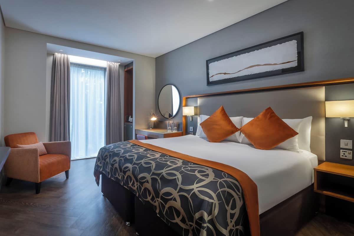 Ein Hotelzimmer mit einem großen Bett, einem Schreibtisch, einem Sessel, einem Fernseher und einem Fenster mit Vorhängen.