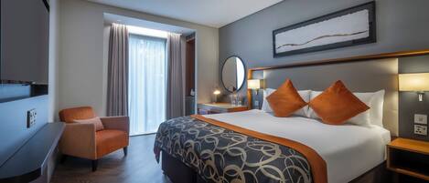 A hotel room with a large bed, a desk, a chair, a TV, and a window with curtains.