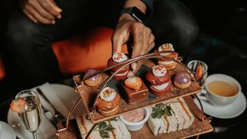 Un plateau contenant un assortiment de viennoiseries et de sandwichs est posé sur une table, accompagné d'une tasse de thé et d'un verre à vin.