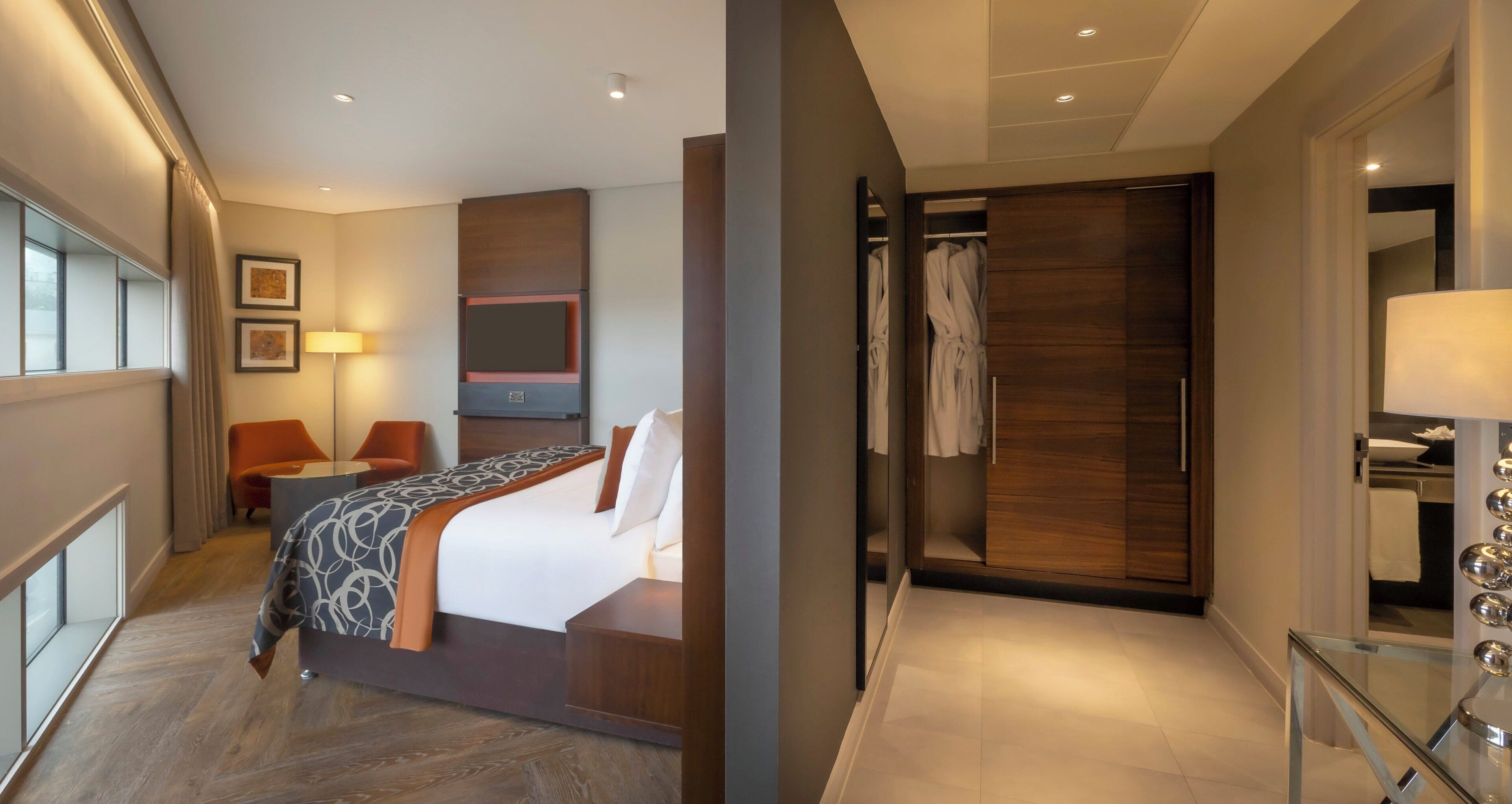 A hotel room with a bed, a seating area with chairs, a vanity with a mirror, and a walk-in closet.