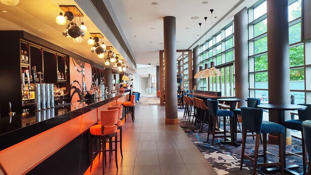 Eine moderne Bar mit einer langen Theke, mehreren Barhocker und einem gemusterten Teppich.