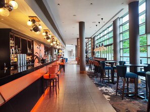 A modern bar area with a long counter, multiple bar stools, and a patterned carpet. - Clayton Hotel Birmingham (Birmingham)