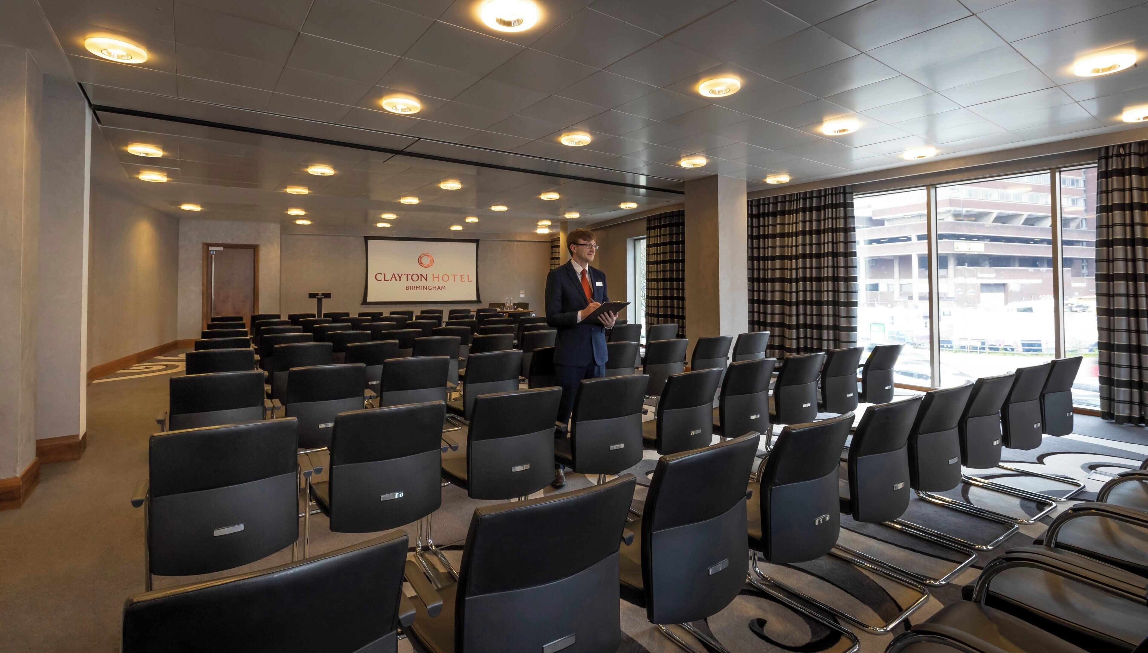 A hotel conference room with rows of chairs, a podium, and a presentation screen.