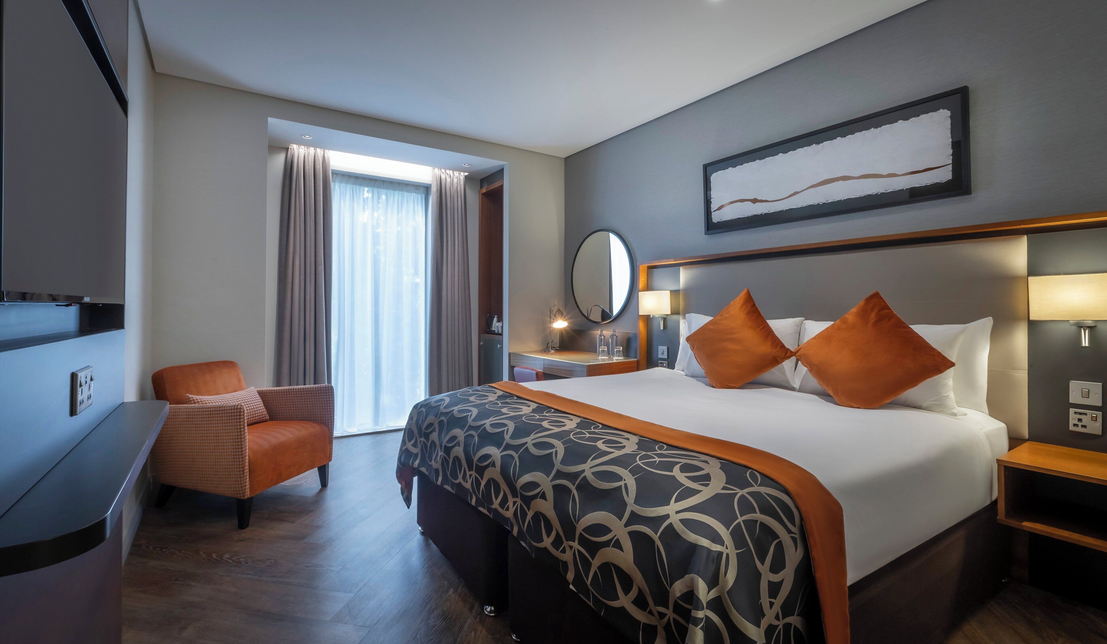 A hotel room with a bed, a desk, a chair, a TV, and a window with curtains.