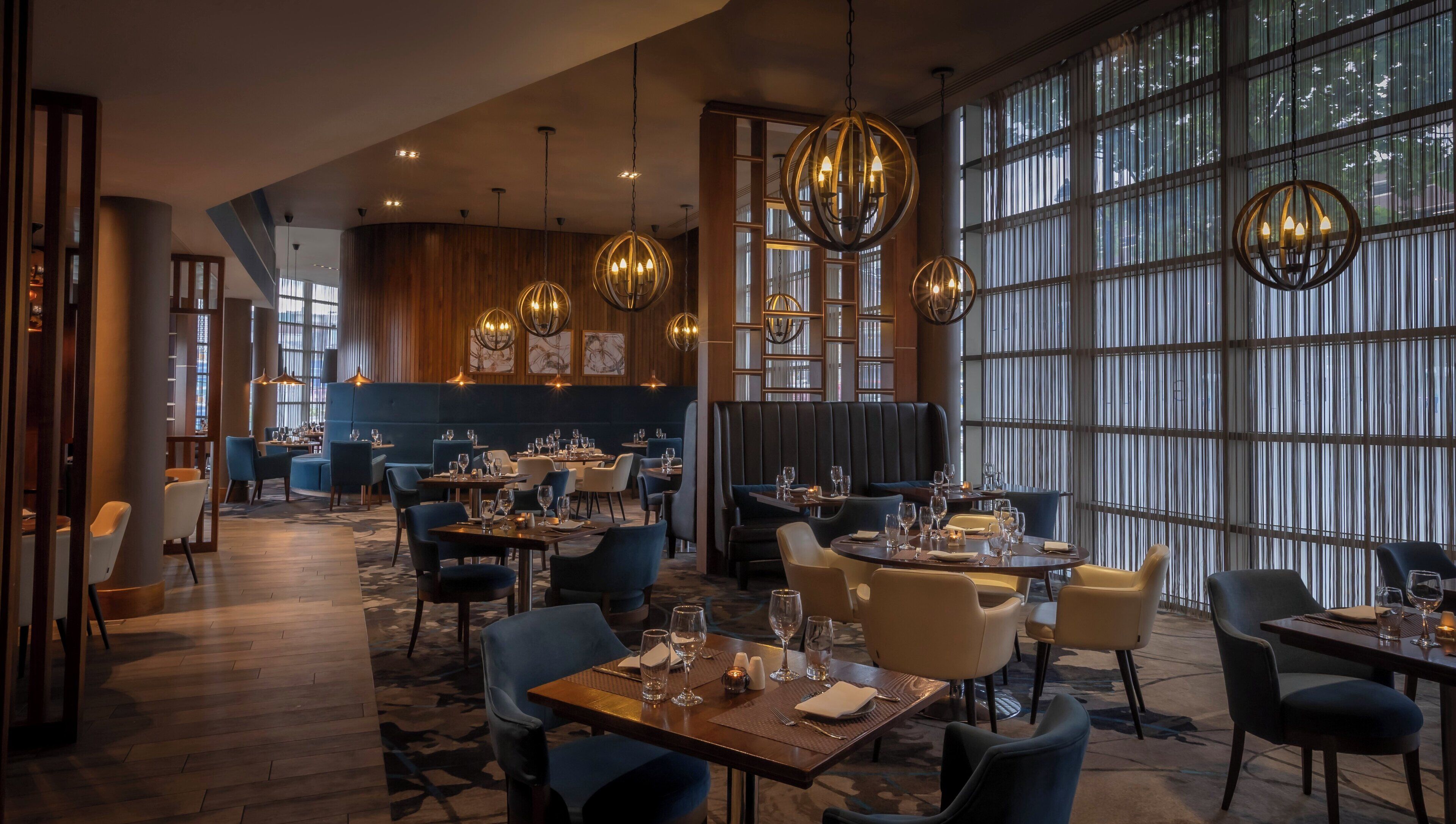 Un restaurant avec de hauts plafonds, des lustres modernes et différents types de sièges, notamment des banquettes et des tables.