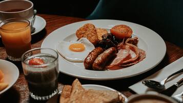 A breakfast setting with a plate of eggs, sausages, bacon, and toast, accompanied by a glass of orange juice and a cup of coffee.