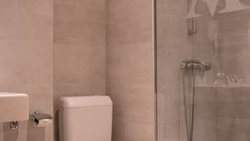 Un baño moderno con inodoro, cabina de ducha de vidrio y un cubo de basura.