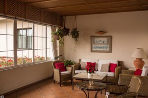 Quarto com móveis de vime, uma mesa de centro de vidro e uma grande janela com flores vermelhas do lado de fora.