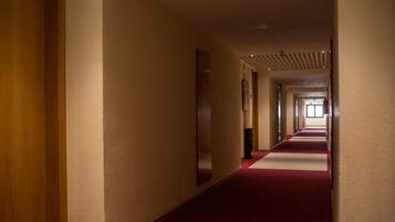 Ein langer, schmaler Hotelgang mit rotem Teppich, Holzwänden und einer Decke mit eingelassenen Leuchten.