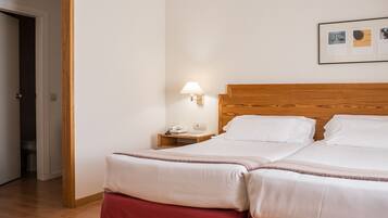 A double bed with white linens, a wooden headboard, a nightstand with a lamp, and a framed picture on the wall.