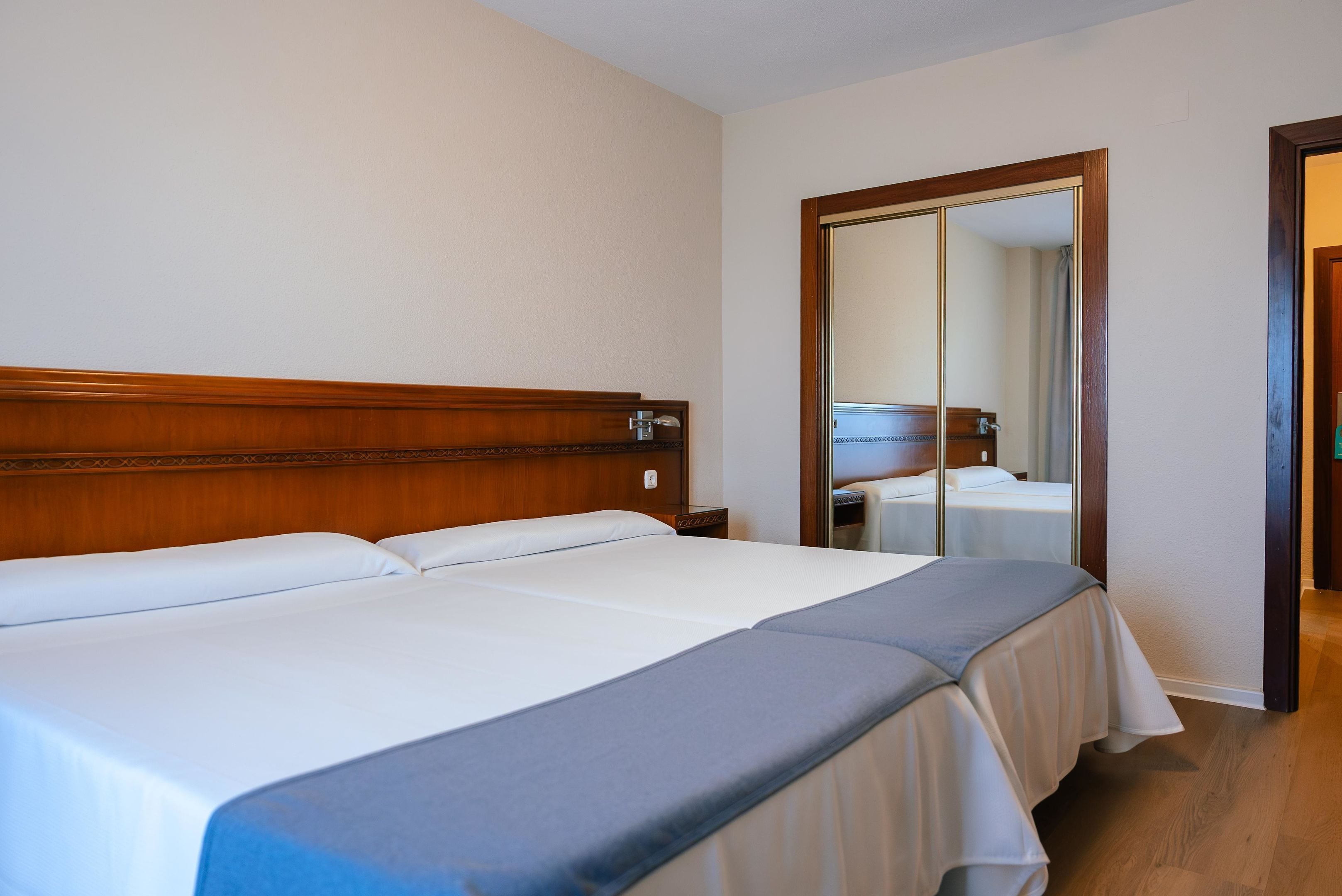 A hotel room with a large bed, wooden headboard, and a mirror on the wall.