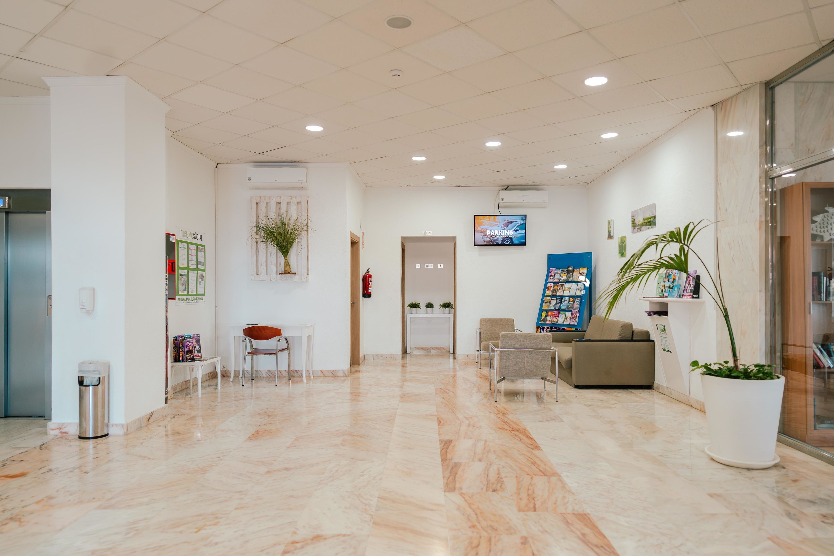 A spacious lobby with a marble floor, seating area, reception desk, and a television screen.