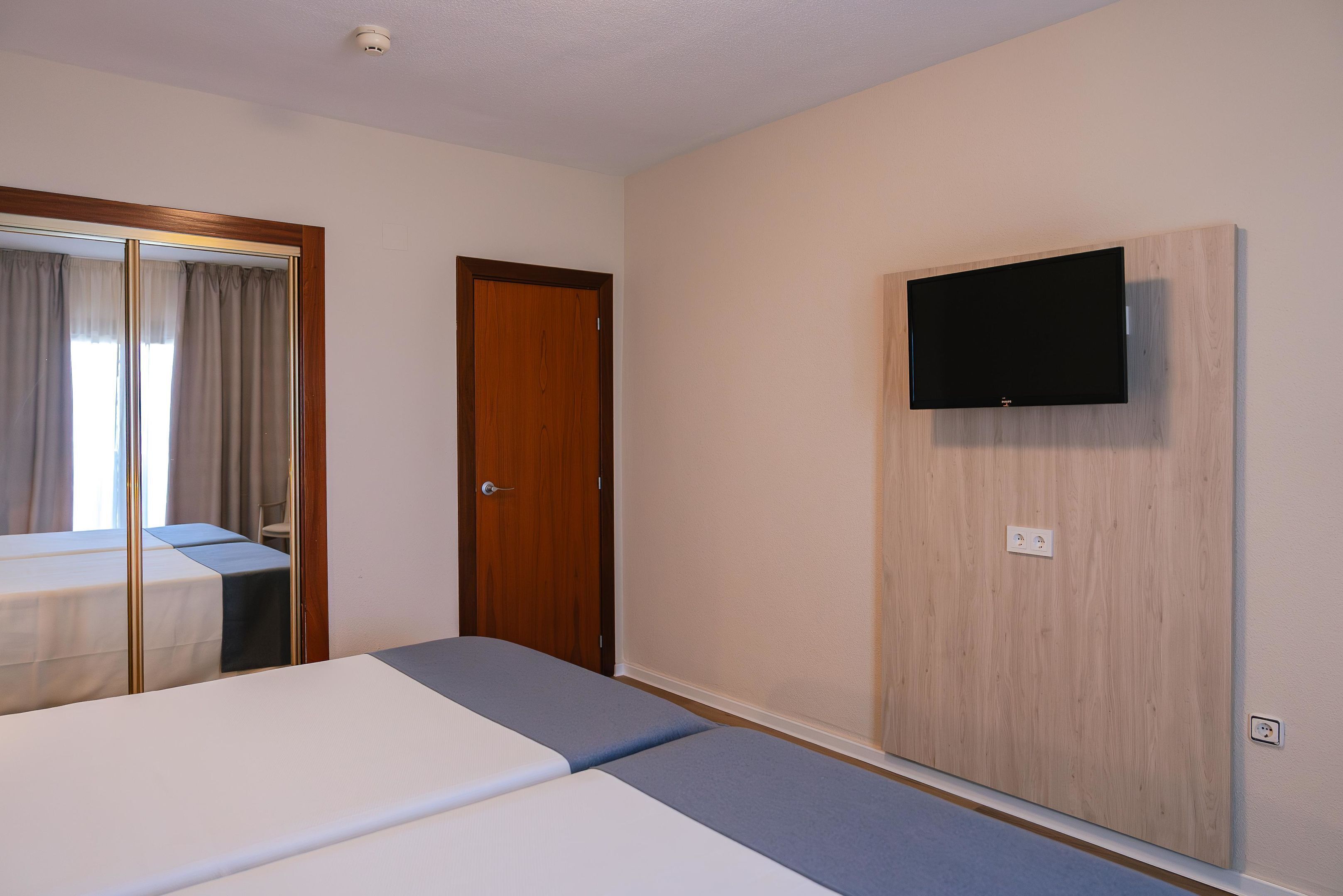 A hotel room with a bed, a TV mounted on the wall, and a door.