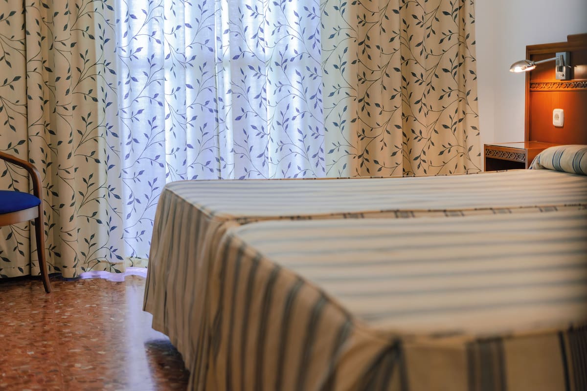 Quarto de hotel com duas camas, uma mesa de cabeceira de madeira, uma escrivaninha e uma cadeira.