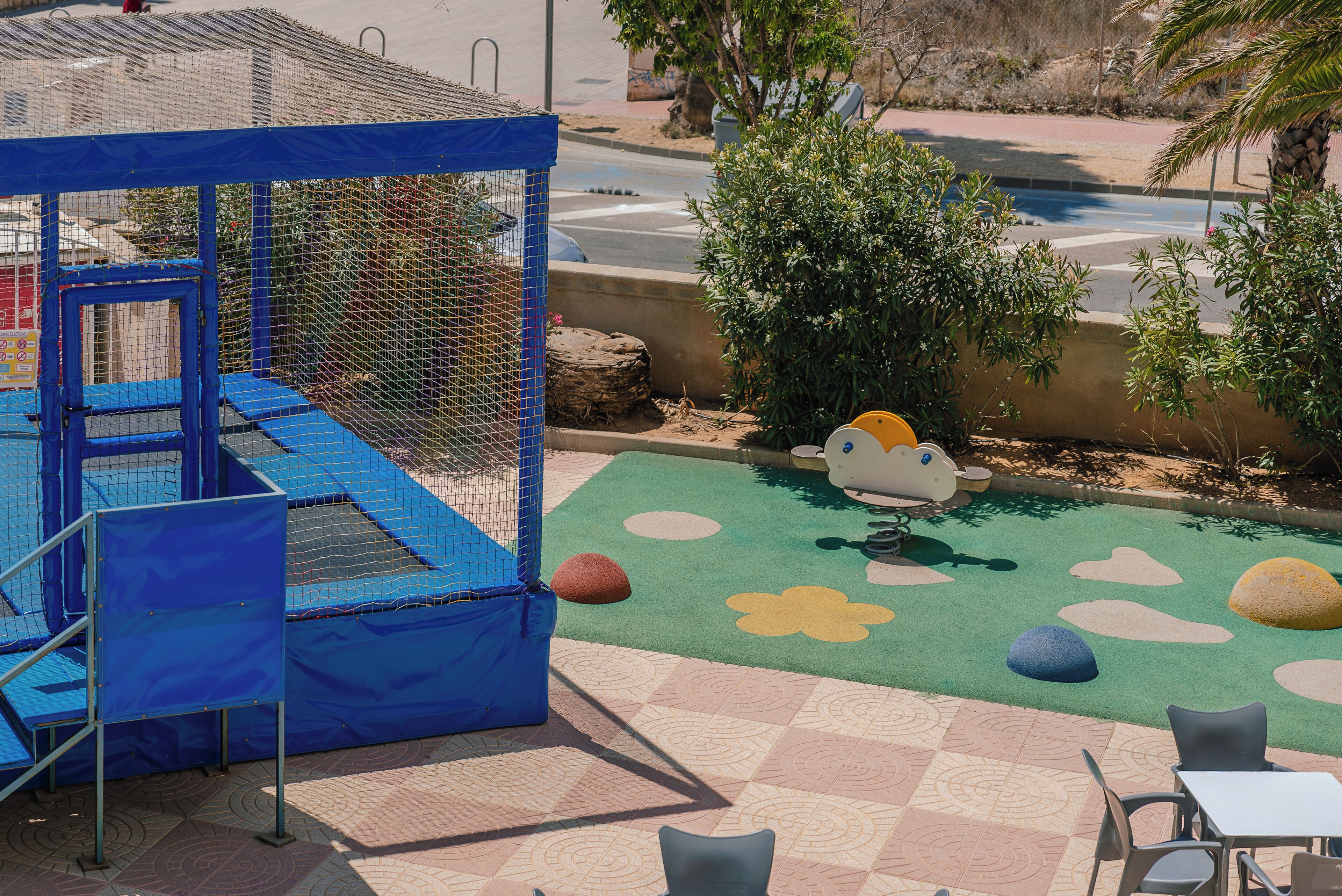 Un espace de jeux avec une structure d’aire de jeux bleue, une piscine et un espace détente équipé de chaises et de tables.