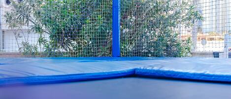 En blå trampolin med net og en væg med runde udskæringer.