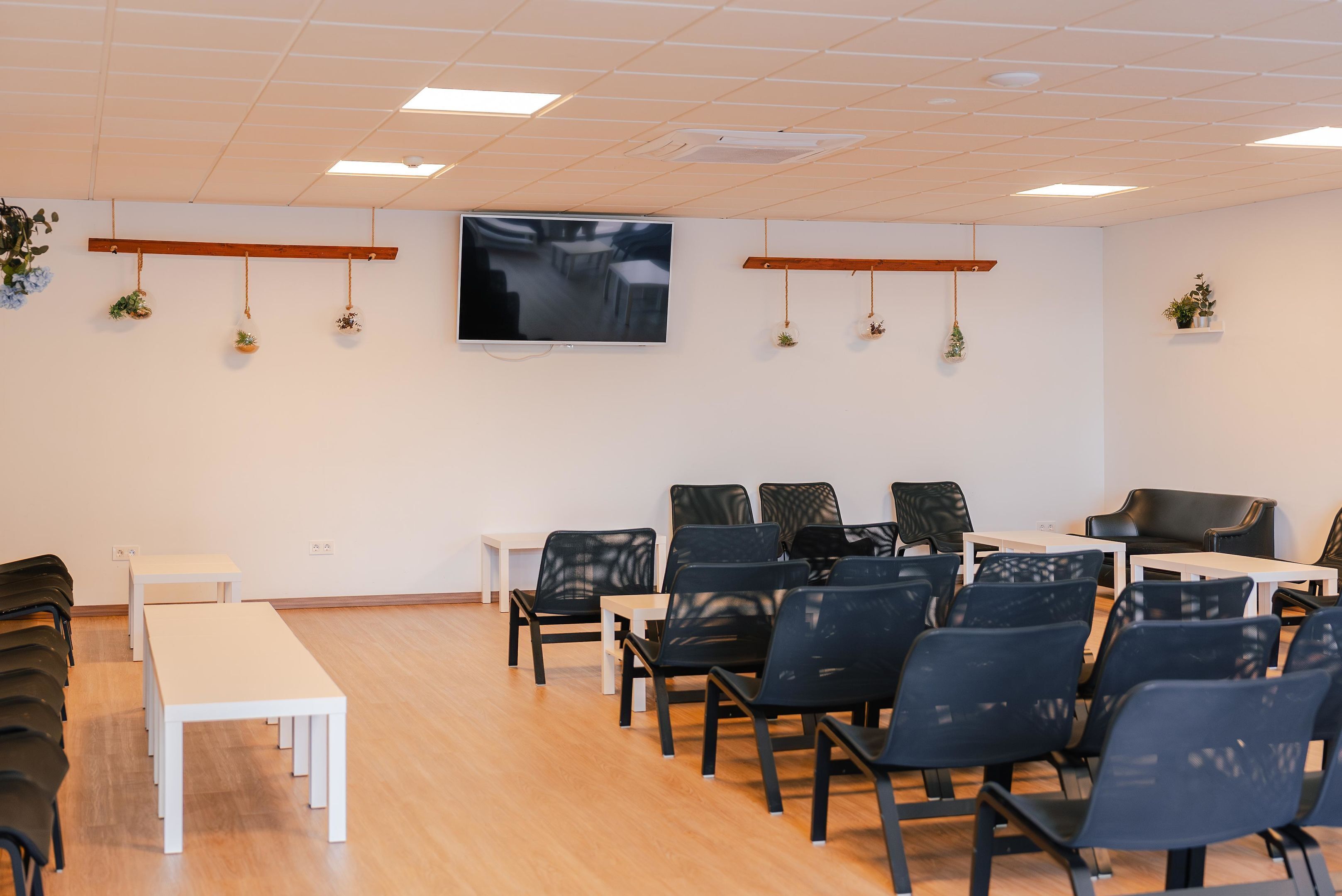 A conference room with a large flat-screen TV, wooden tables, and chairs arranged for meetings.
