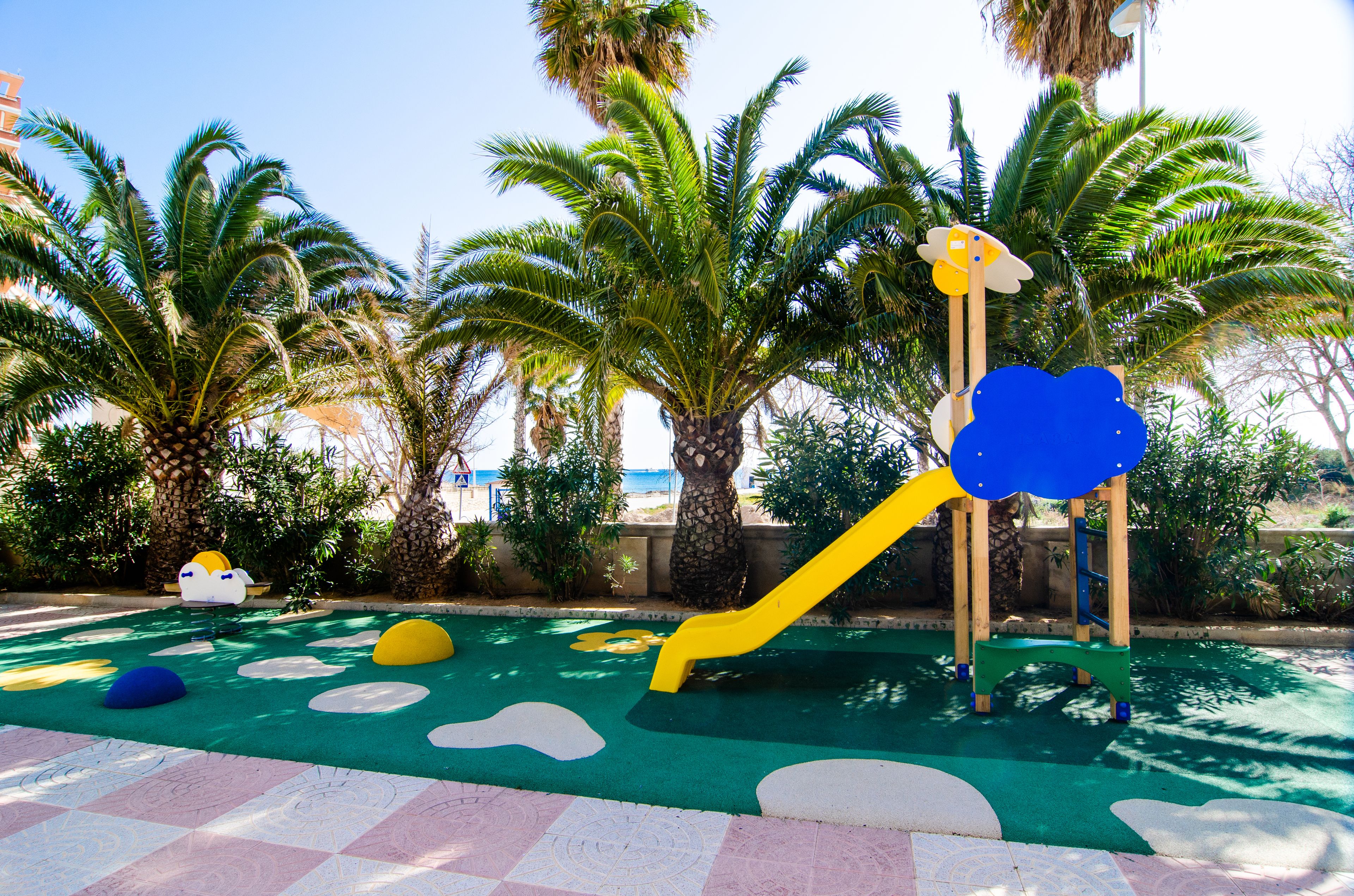 A playground with a slide, climbing structure, and colorful ground surface.