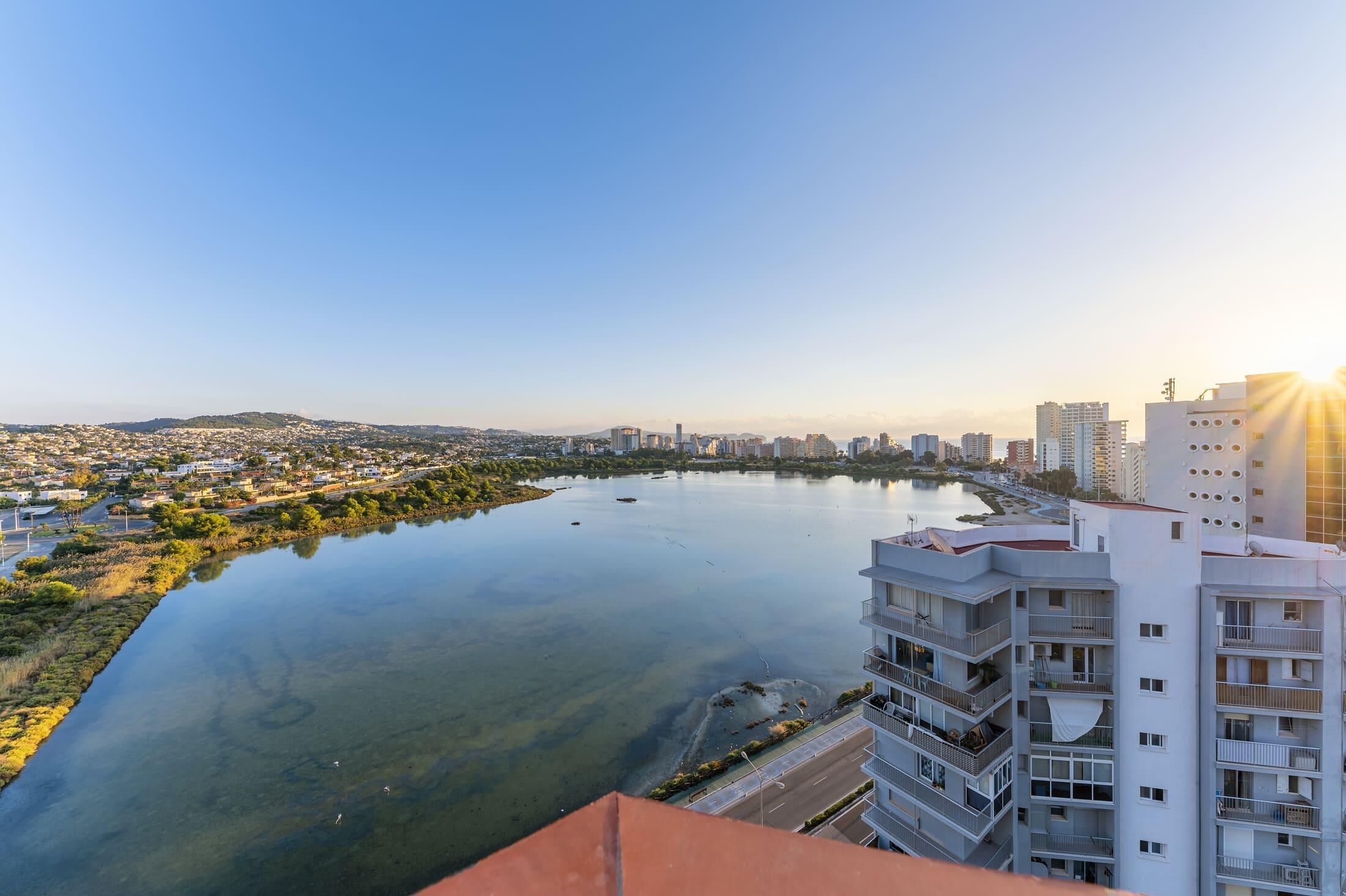 Un edificio alto con varios balcones que dan a un río tranquilo y a un paisaje urbano.