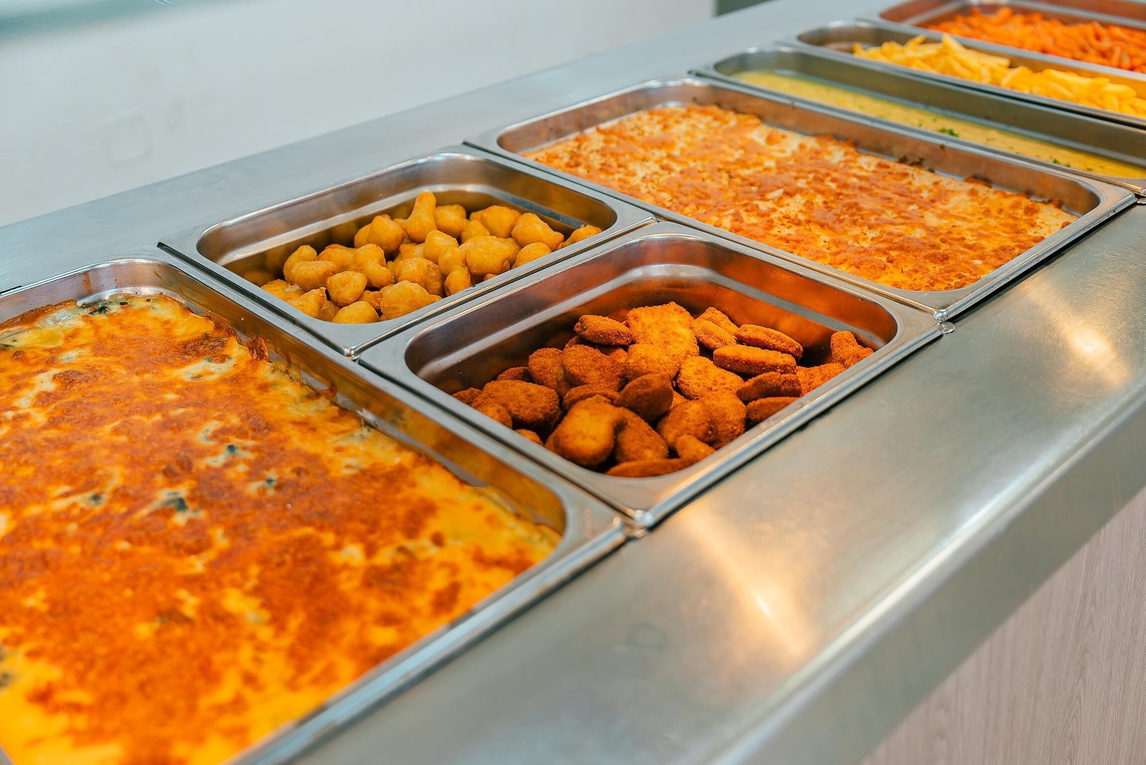 Ein reichhaltiges Buffet mit verschiedenen Speisen, darunter eine Auflaufform, Kartoffelwürfel und gebratenes Hähnchen.