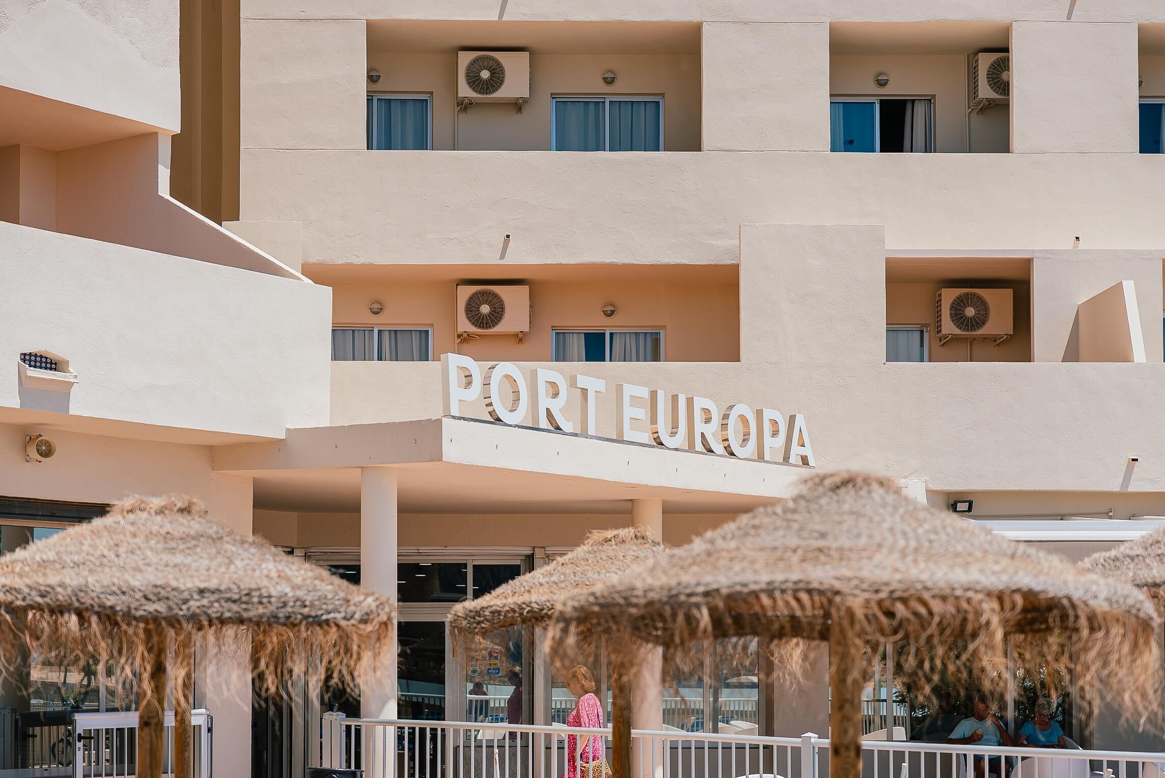 Un hotel llamado "PORTEEUROPA" con varios balcones, unidades de aire acondicionado y sombrillas exteriores.