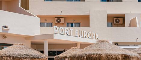 Hotel chamado "PORTEEUROPA" com várias varandas, aparelhos de ar condicionado e guarda-sóis de exterior.