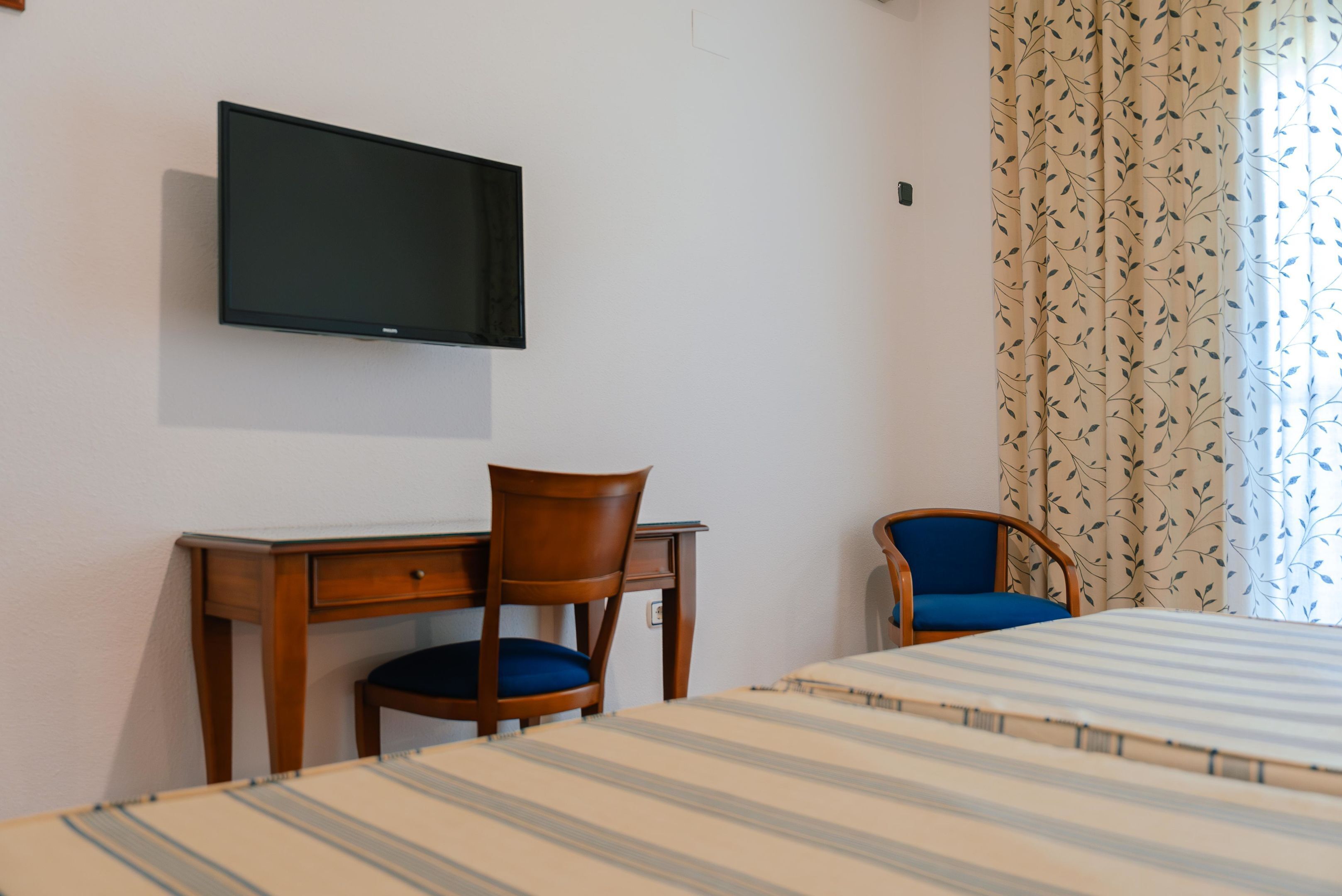 Une chambre d’hôtel comprenant un lit, un bureau avec une chaise, un téléviseur fixé au mur et une fenêtre avec des rideaux.