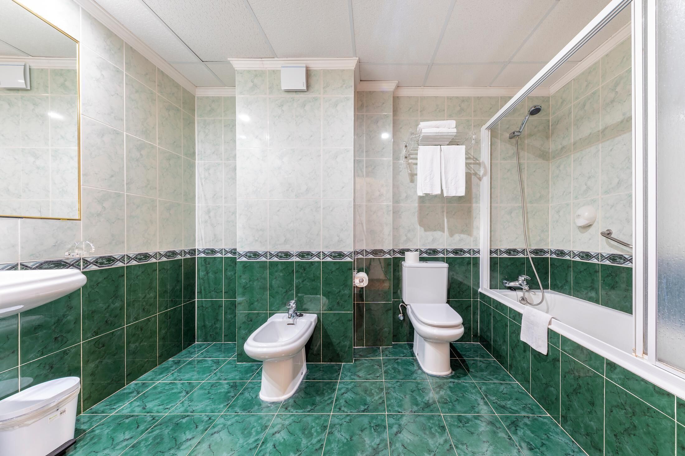Ein Badezimmer mit grünen Marmorfliesen, einem Bidet, einer Toilette und einer Dusche.