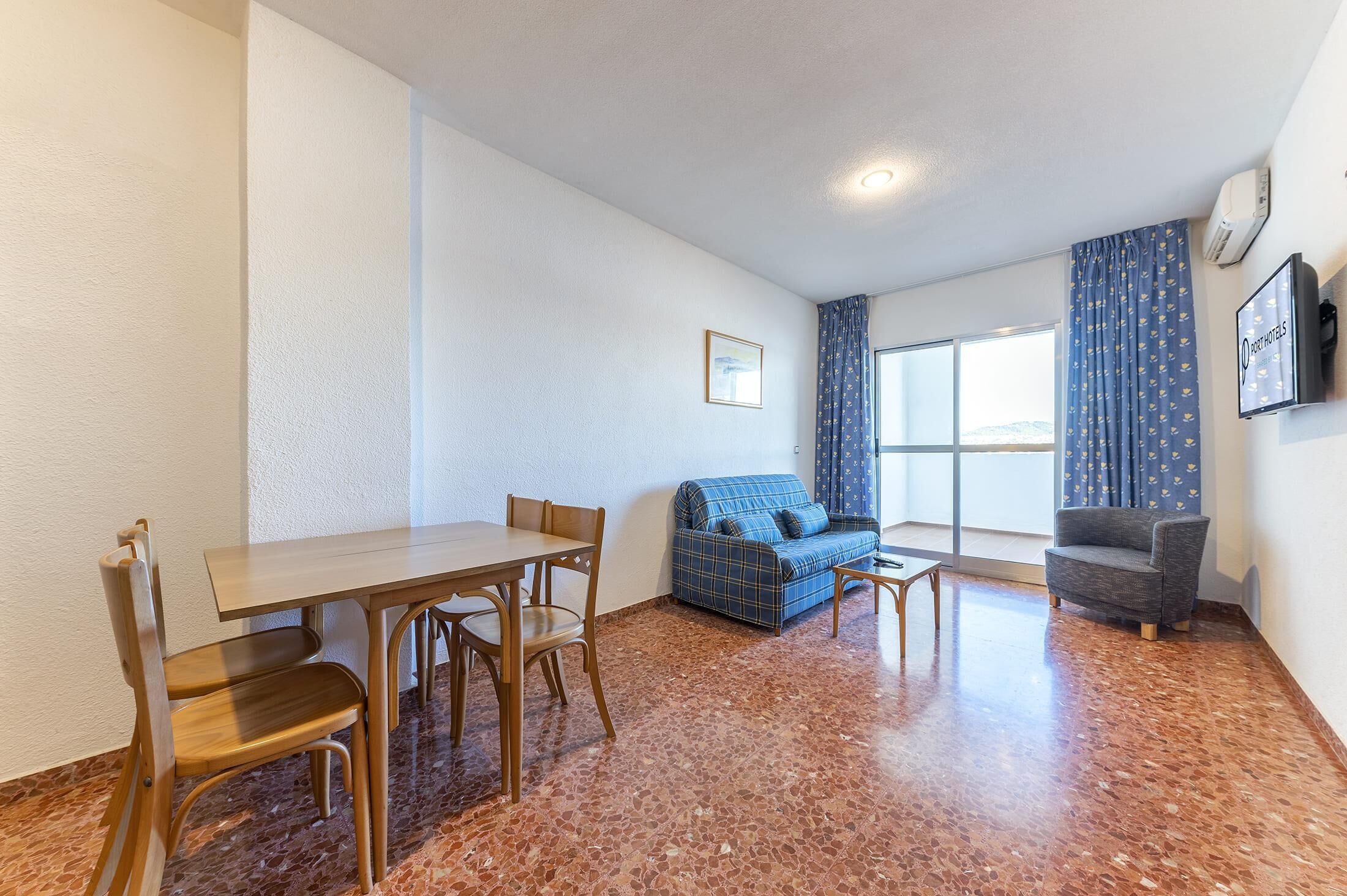 Una habitación con una mesa de comedor y sillas, un sofá, una mesita y un televisor en la pared.
