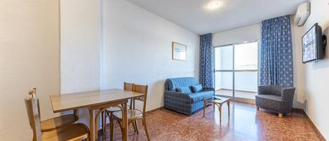 Una habitación con una mesa de comedor y sillas, un sofá, una mesita y un televisor en la pared.