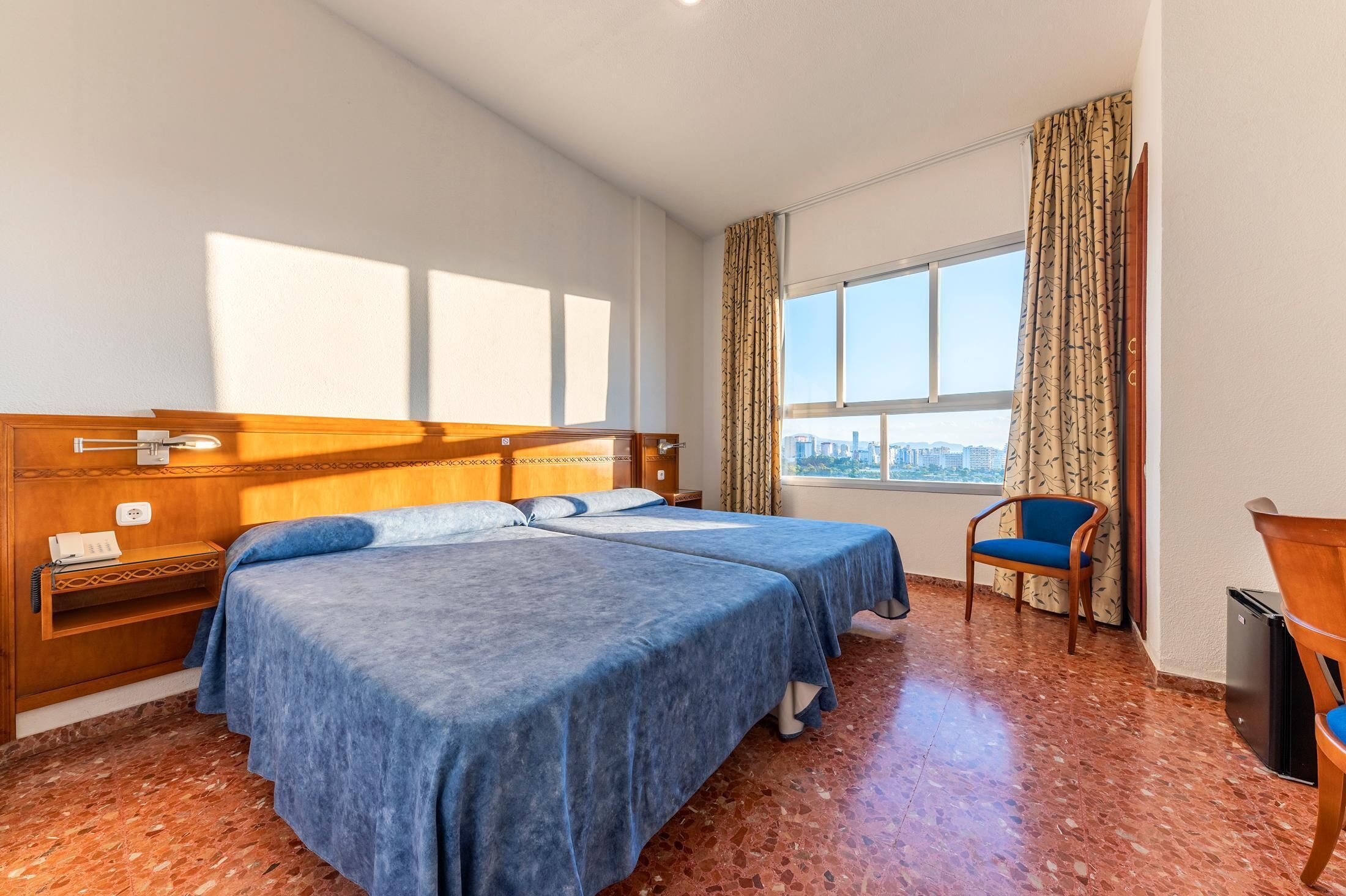 A hotel room with two beds, a city view, a wooden headboard, a chair, and a trash bin.