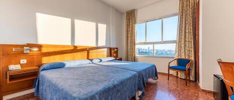 A hotel room with two beds, a city view, a wooden headboard, a chair, and a trash bin.
