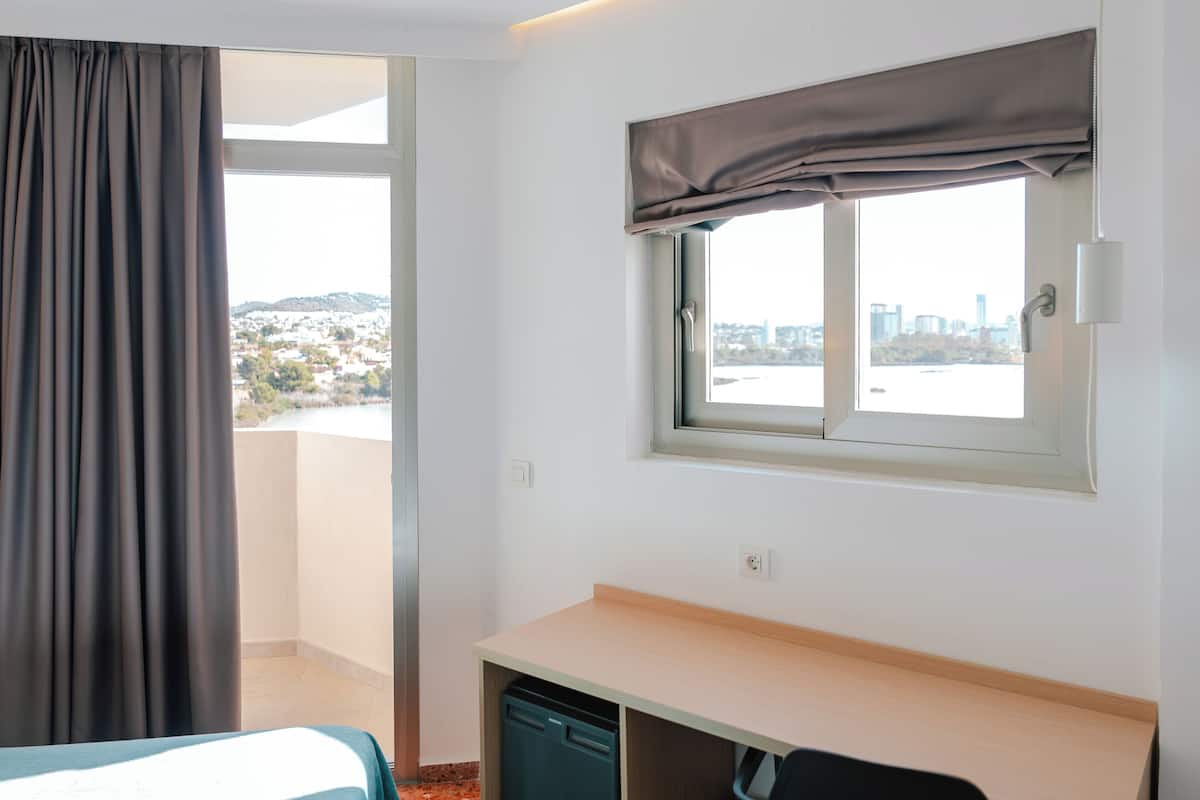 Quarto de hotel com cama, escrivaninha, janela com vista para a paisagem urbana e cortina.