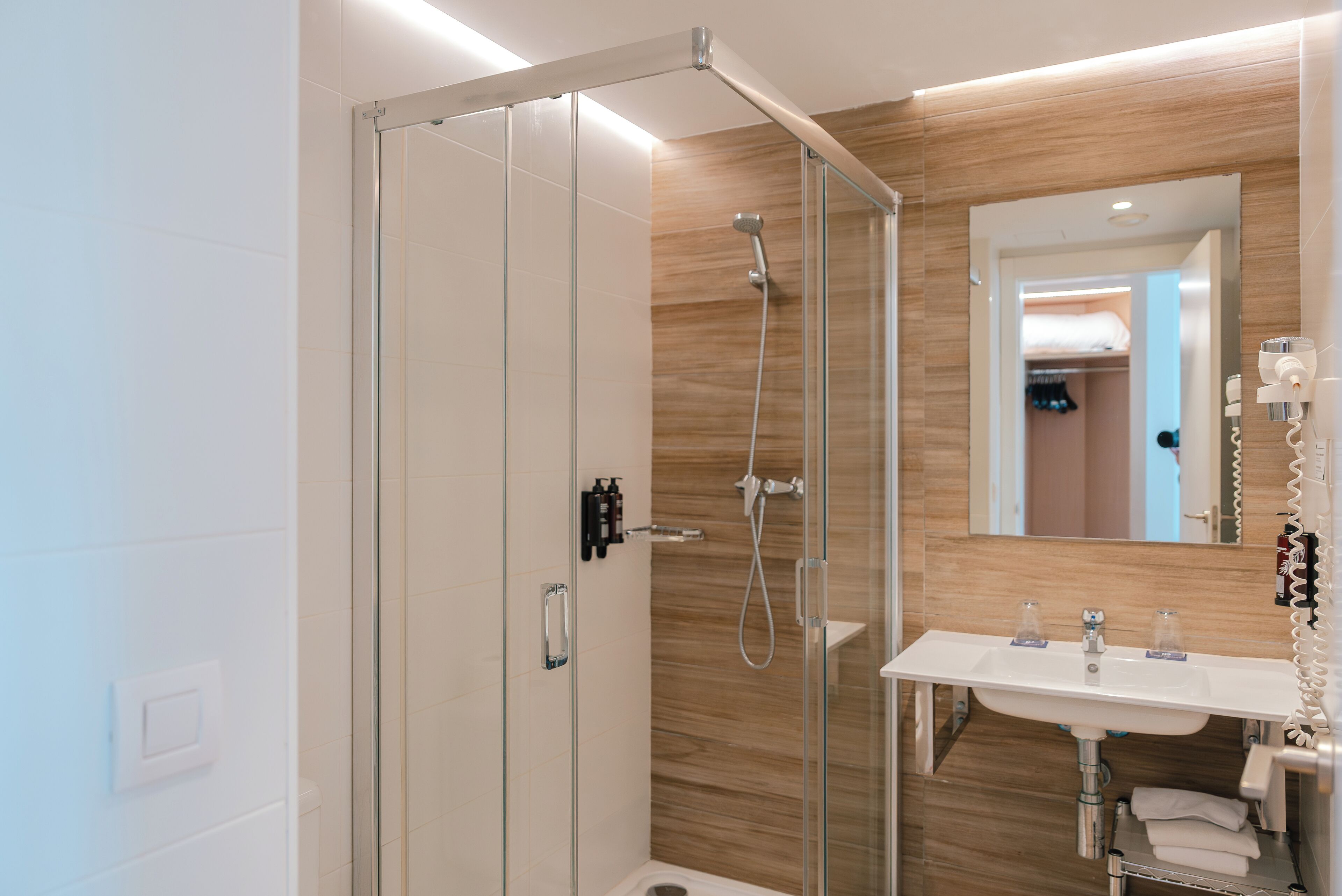 Un baño moderno con ducha envuelta en cristal, un lavabo blanco con espejo y una pared de madera.