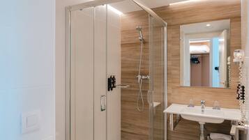 Un baño moderno con ducha envuelta en cristal, un lavabo blanco con espejo y una pared de madera.