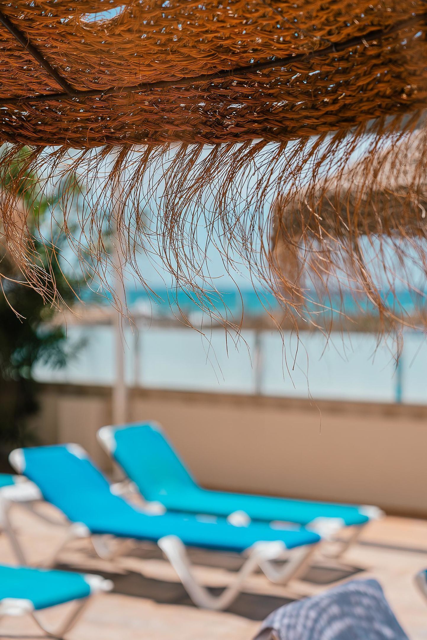 Una sombrilla de playa con un diseño tejido y una zona junto a la piscina con sillas reclinables azules.