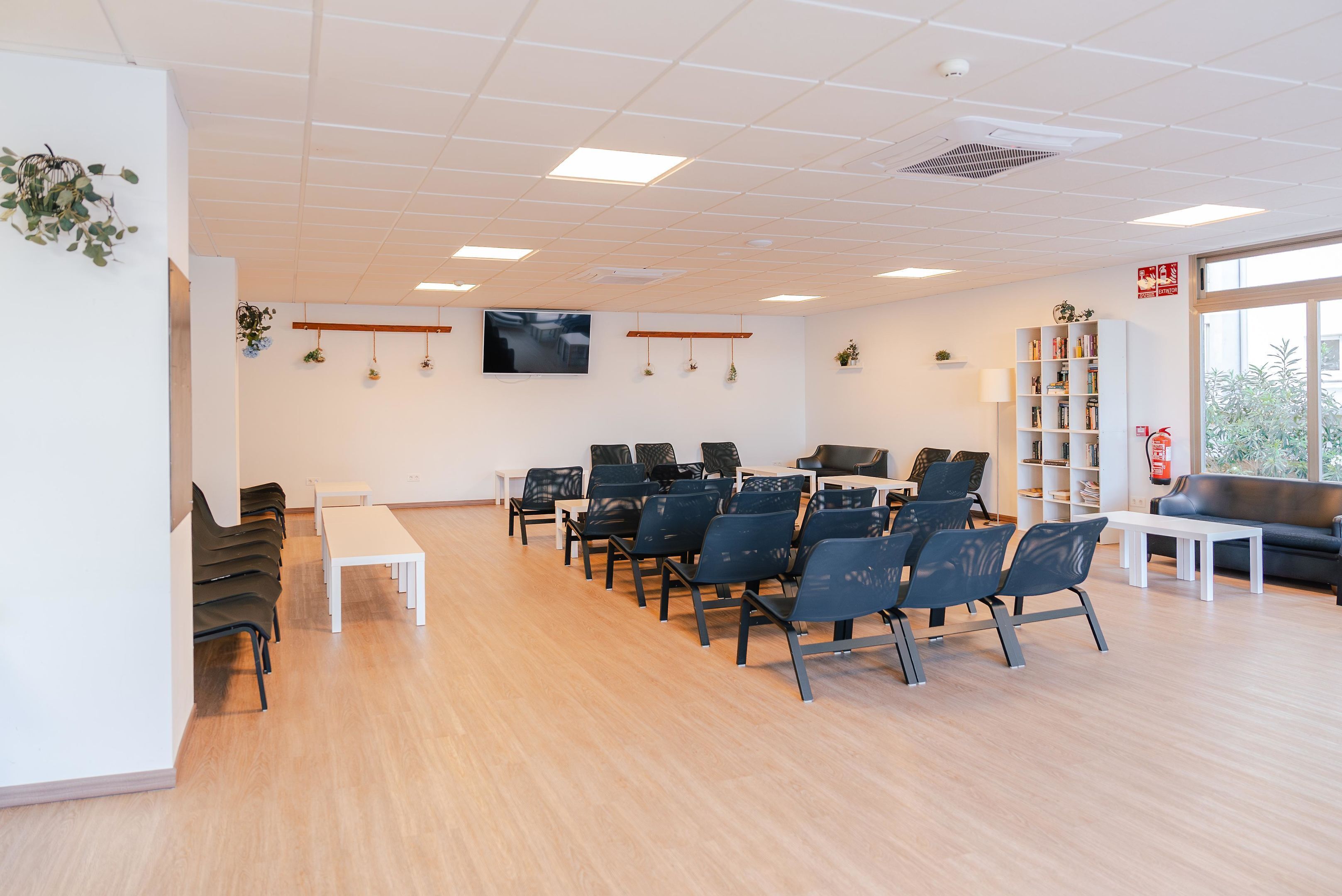 Un salón de conferencias moderno con filas de sillas, una mesa blanca y una estantería.