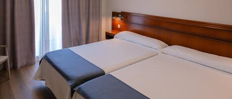 A hotel room with two beds, a wooden headboard, a nightstand, and a window with curtains.
