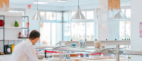 A buffet area with multiple food stations, a person serving food, and hanging pendant lights.