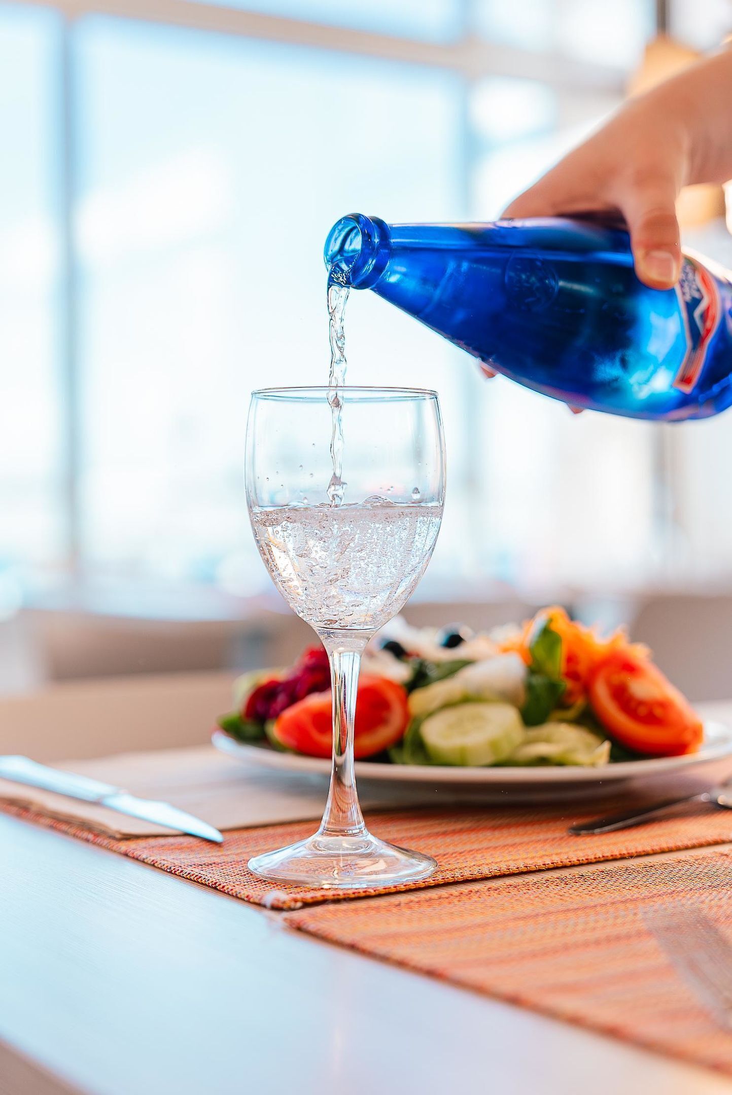 A hand pouring water into a clear glass.