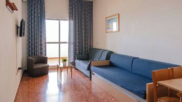 A compact living space with a sofa, a chair, a small table, and a window with curtains.