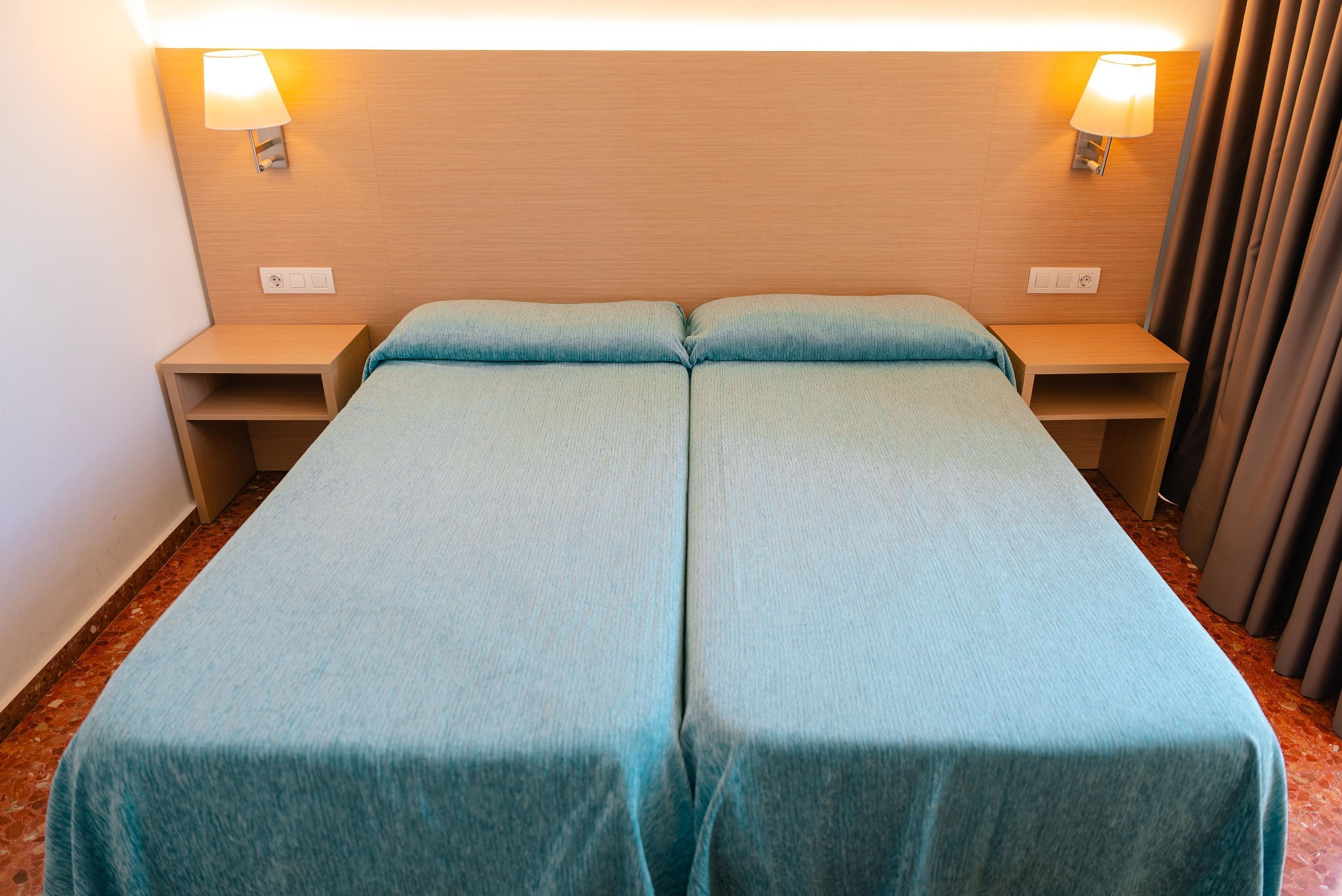 Una cama doble con una colcha azul claro, dos mesitas de noche con lámparas y un cabecero de madera.