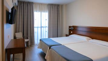Quarto de hotel com duas camas, uma escrivaninha, uma cadeira, uma televisão e uma janela com cortinas.