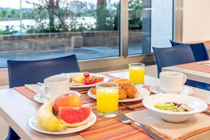 A breakfast setting with a table set for two, including plates with fruit, croissants, and a bowl of cereal. - Port Europa Hotel (Calpe)