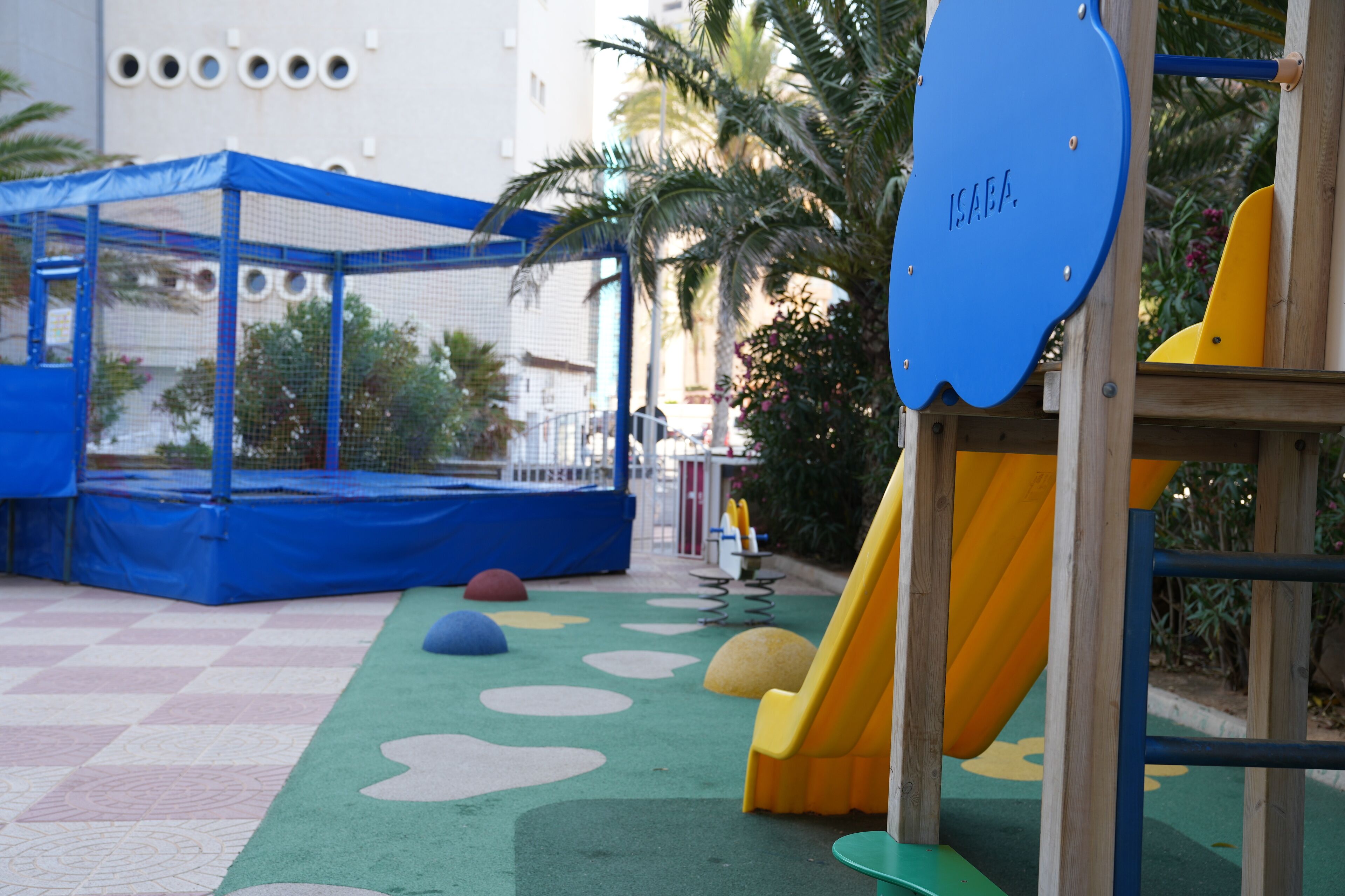 A children's play area with a slide, climbing net, and colorful play mats.