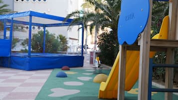 Zona de juegos infantiles con un tobogán, red de escalada y alfombras de colores.