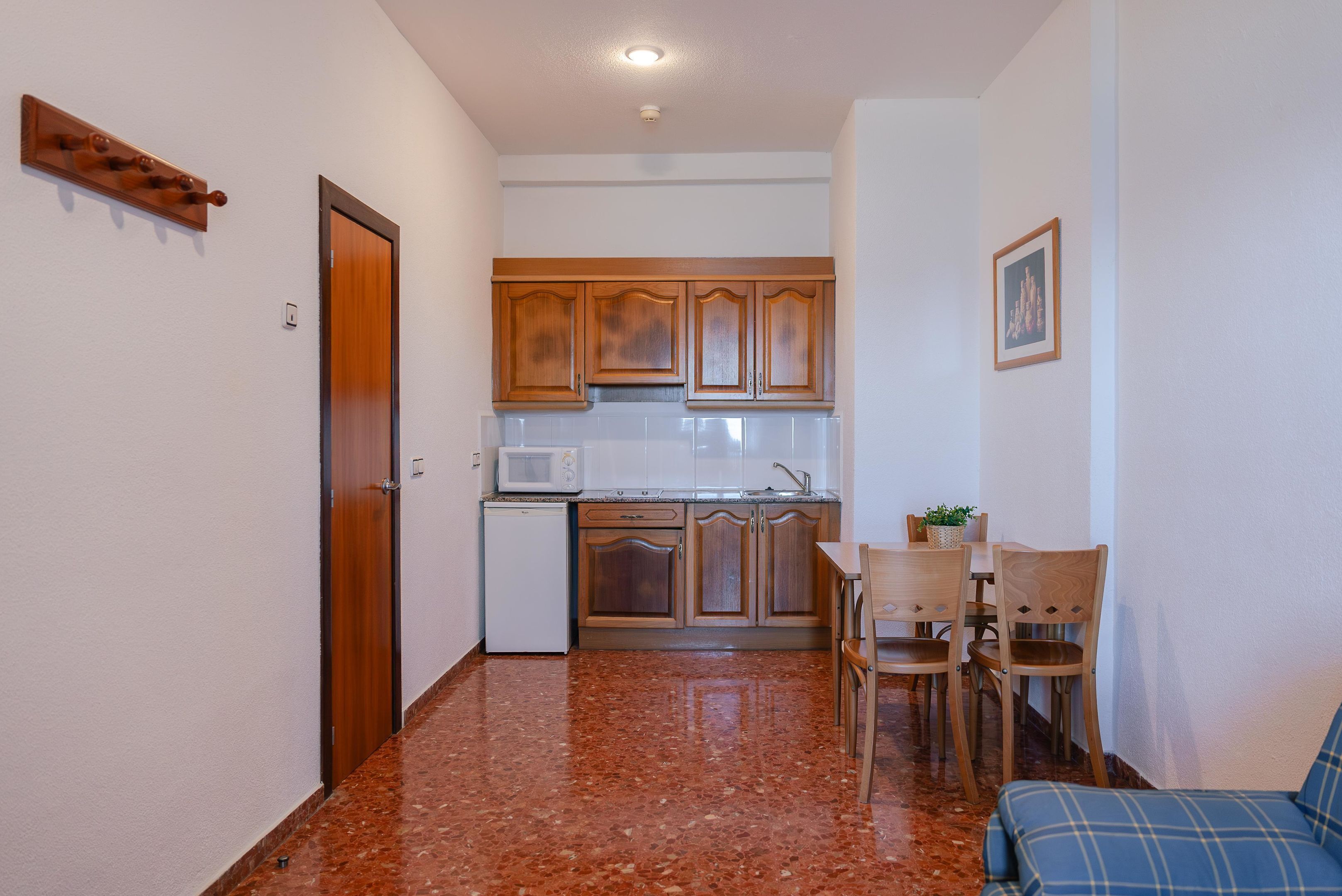 A compact kitchen with wooden cabinets, a microwave, and a sink. There is a dining area with a table and chairs.